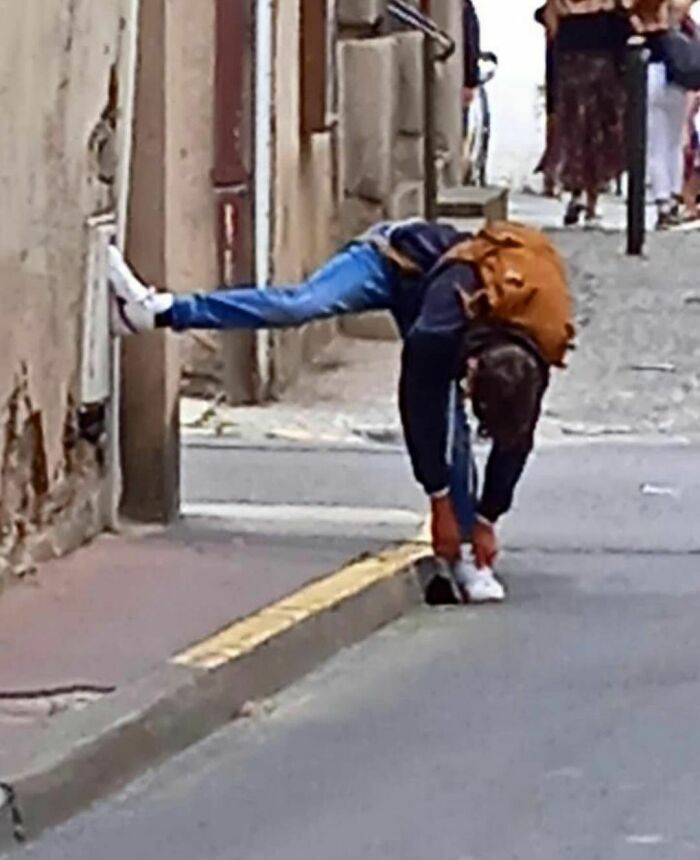 Person bending down to tie shoe while balancing with one leg on a wall in a random and cringe photo moment