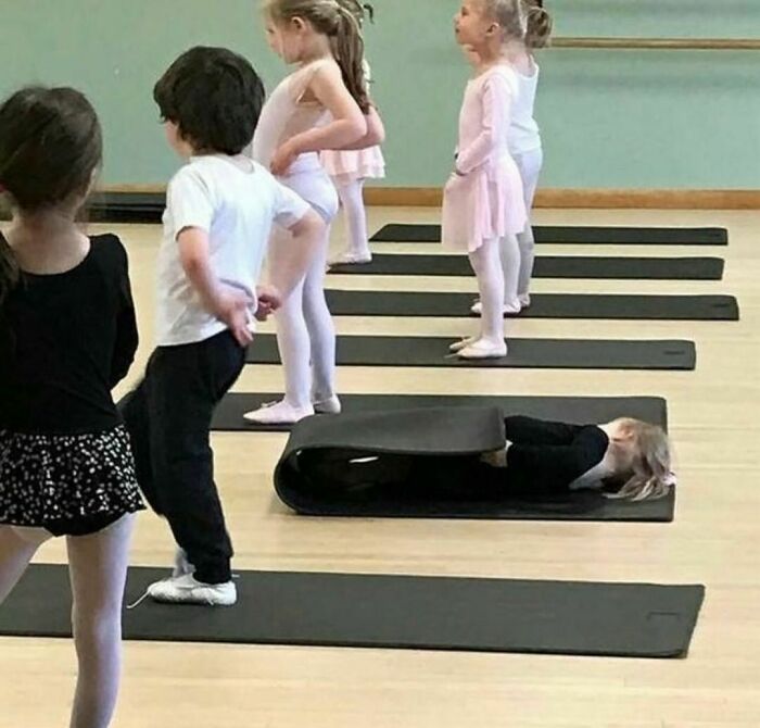 A child wrapped inside a folded exercise mat during a dance class, showing a random and cringe moment.