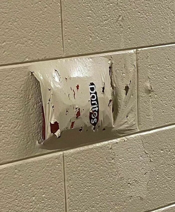 Doritos chip bag melted and fused onto a tiled wall, creating a random and cringe humorous visual effect.