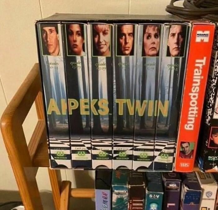 VHS tapes on a wooden shelf with a misaligned cover spelling APEKS TWIN, a random and cringe photo.