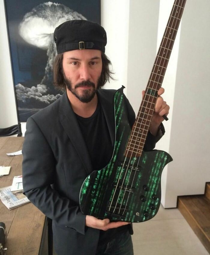 Man wearing a black hat and blazer holding a bass guitar with a unique green pattern in a modern room random cringe photo