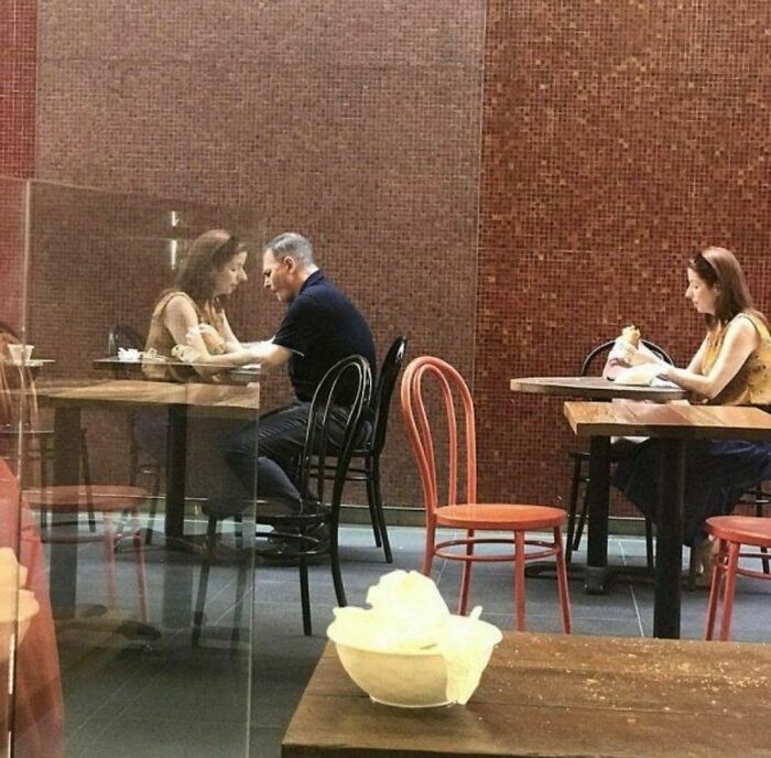 Two people sitting at a table reflected in glass creating a random and cringe photo effect with a unique sense of humor.