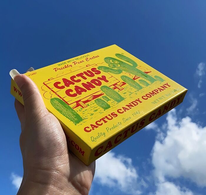 Hand holding a bright yellow box of cactus candy against a clear blue sky, showcasing unique snack packaging. Hand holding a bright yellow box of cactus candy against a clear blue sky, showcasing unique snack packaging.