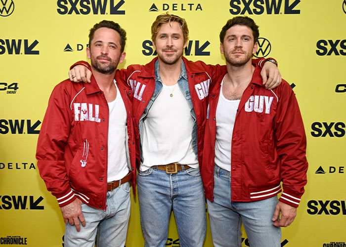 Ryan Gosling at SXSW event, wearing a red jacket and jeans, posing with two men, showcasing style changes. Ryan Gosling at SXSW event, wearing a red jacket and jeans, posing with two men, showcasing style changes.