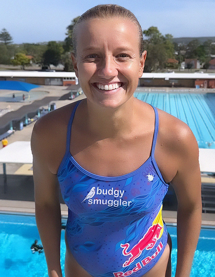 Female thrill-seeking diver in swimsuit smiling at poolside before extreme waterslide jump. Female thrill-seeking diver in swimsuit smiling at poolside before extreme waterslide jump.
