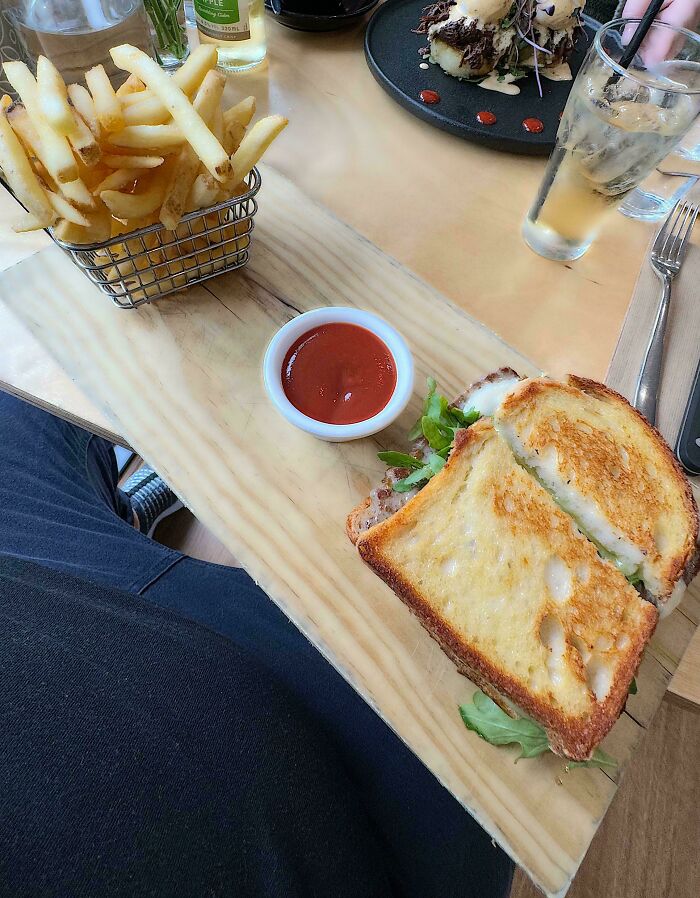 Sandwich and fries served on a wooden board with ketchup, showcasing one of the most ridiculous ways people had food served in restaurants.