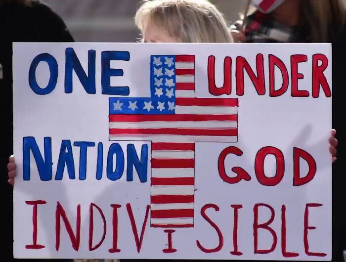 Person holding a sign with a humorous message layout fail using US flag colors and the words "ONE NATION UNDER GOD INDIVISIBLE."