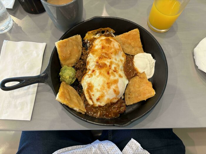Cast iron skillet used to serve Mexican food with meat, cheese, guacamole, and chips in a restaurant setting.