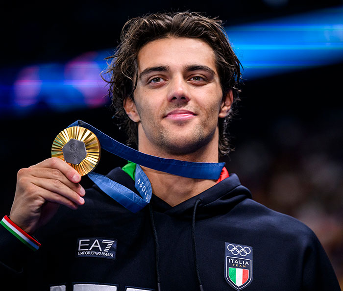Gold medalist in black hoodie holding medal at an event. Gold medalist in black hoodie holding medal at an event.