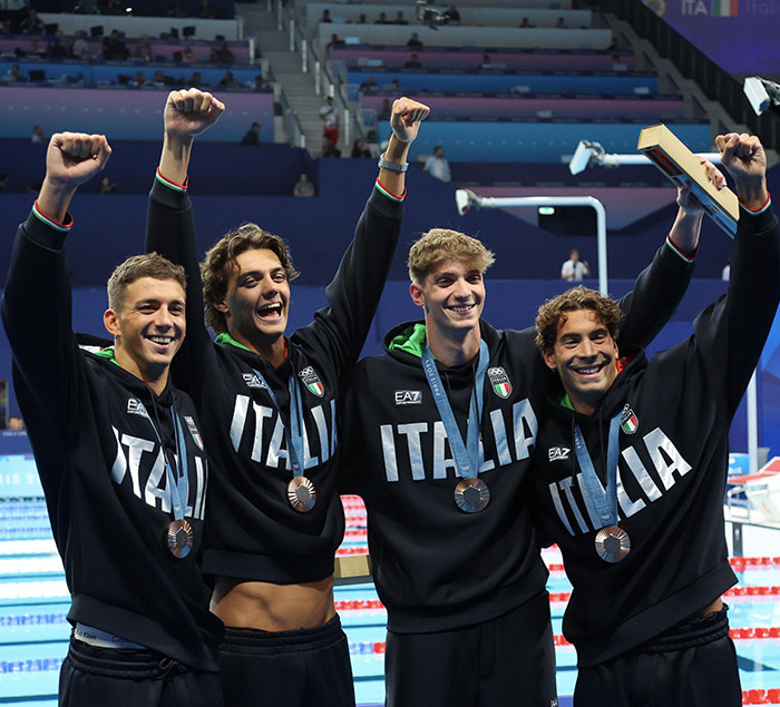 Four Italian swimmers celebrate with medals around their necks, cheering on the podium. Four Italian swimmers celebrate with medals around their necks, cheering on the podium.