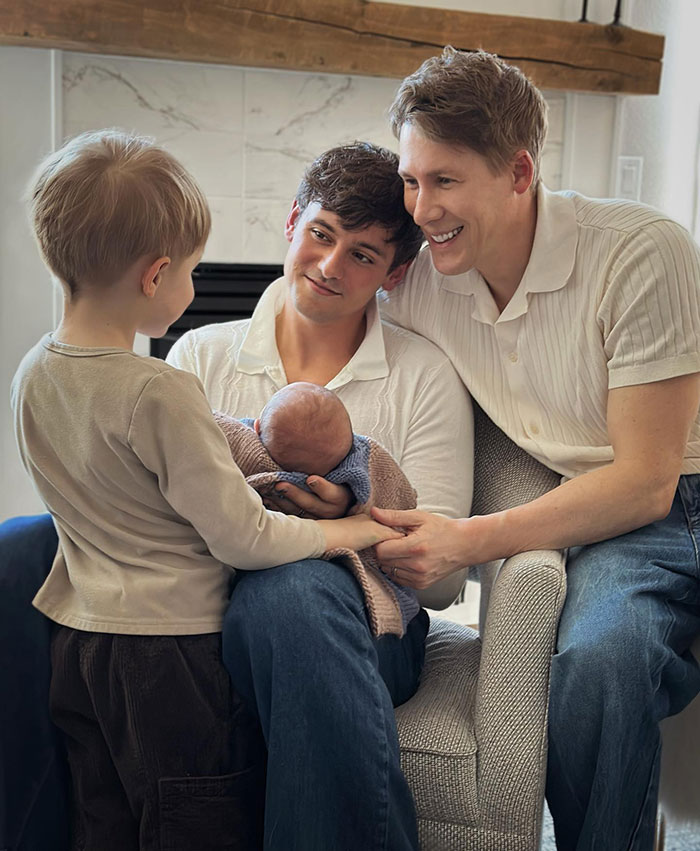 A happy family gathers as a man in a white shirt holds a baby, while another man and a child look on with smiles. A happy family gathers as a man in a white shirt holds a baby, while another man and a child look on with smiles.