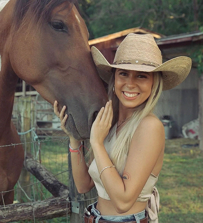 Young woman in a cowboy hat smiling beside a horse in a rural setting. Young woman in a cowboy hat smiling beside a horse in a rural setting.