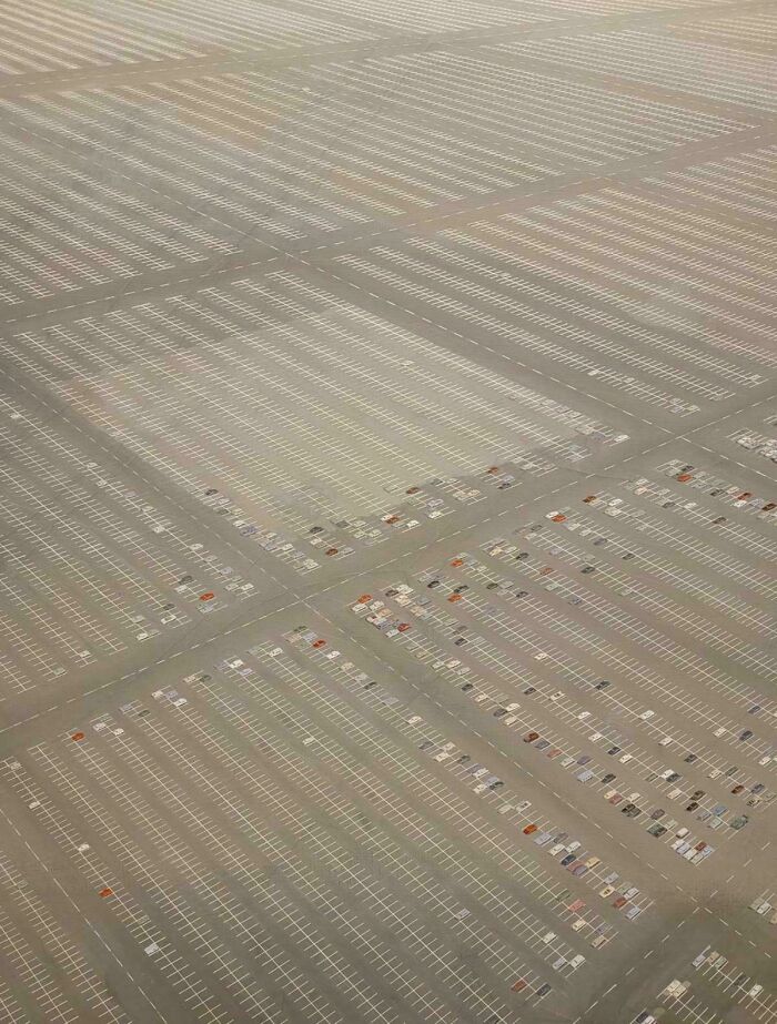 Aerial view of an enormous empty parking lot with few scattered cars, creating a sense of vast scale for megalophobia.