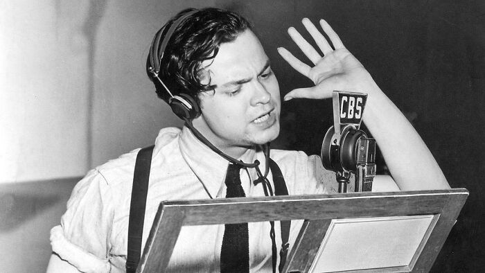 Black and white photo of a vintage radio broadcaster speaking into CBS microphone, reminding you of creaking joints nostalgia.