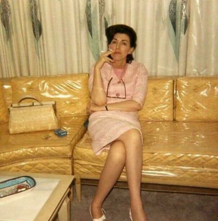 Woman in pink vintage dress sitting on retro vinyl couch, evoking nostalgia and creaking joints memories.