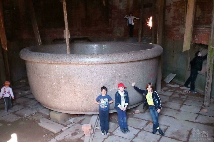 Children standing next to an enormous stone bathtub in a dimly lit old building, evoking megalophobia fears.