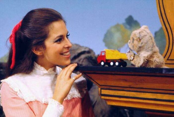 Woman smiling at a vintage toy truck held by a puppet bear, recalling nostalgic items that remind you of creaking joints.