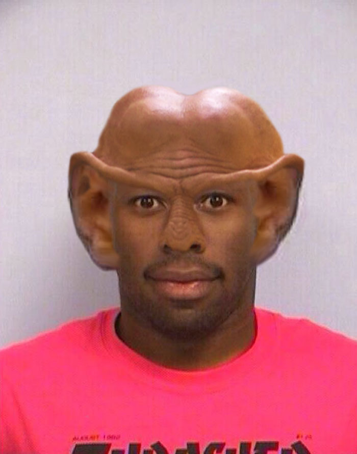 Tyler The Creator mugshot with alien features, large forehead, pointy ears, wearing a pink shirt. Tyler The Creator mugshot with alien features, large forehead, pointy ears, wearing a pink shirt.