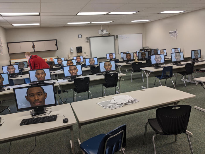 Computer lab monitors displaying Tyler The Creator mugshot, person in red hoodie adjusting a computer. Computer lab monitors displaying Tyler The Creator mugshot, person in red hoodie adjusting a computer.