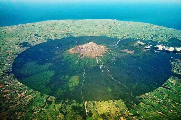 Aerial view of a massive volcanic mountain casting a large shadow, evoking fear for those with megalophobia.