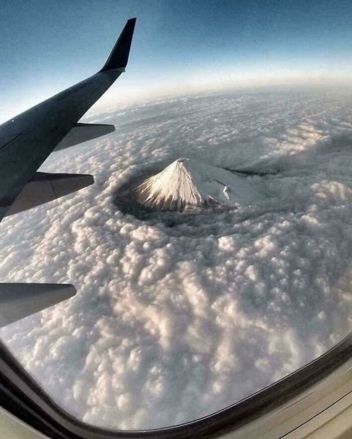 View from airplane window showing a giant snow-capped mountain surrounded by thick clouds evoking megalophobia fear.