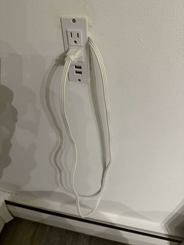 Electrical outlet with two flat cables plugged in, showing a DIY disaster with wiring in a home setting.