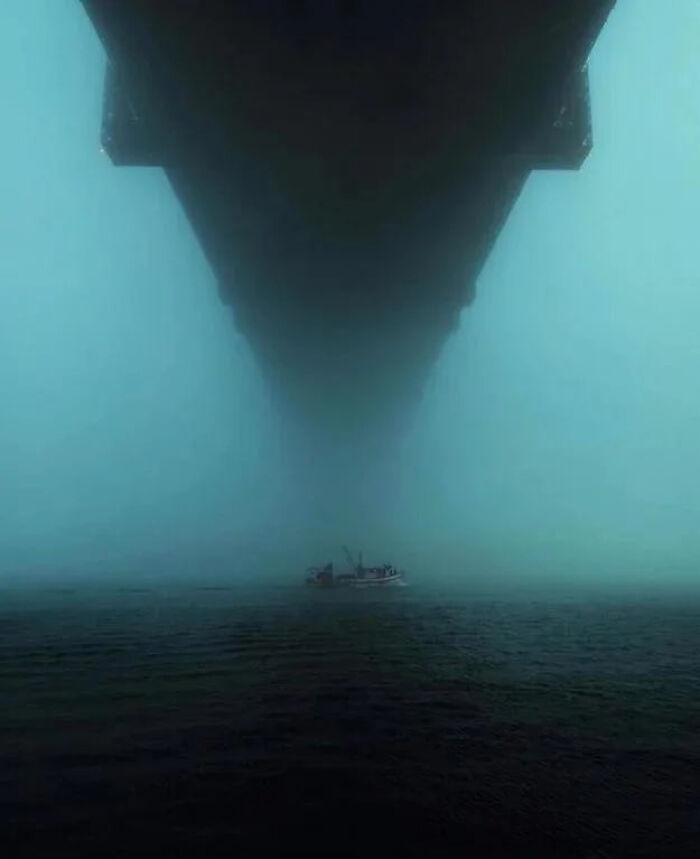 Massive structure looming over small boat in foggy water scene evoking strong fear for those with megalophobia.