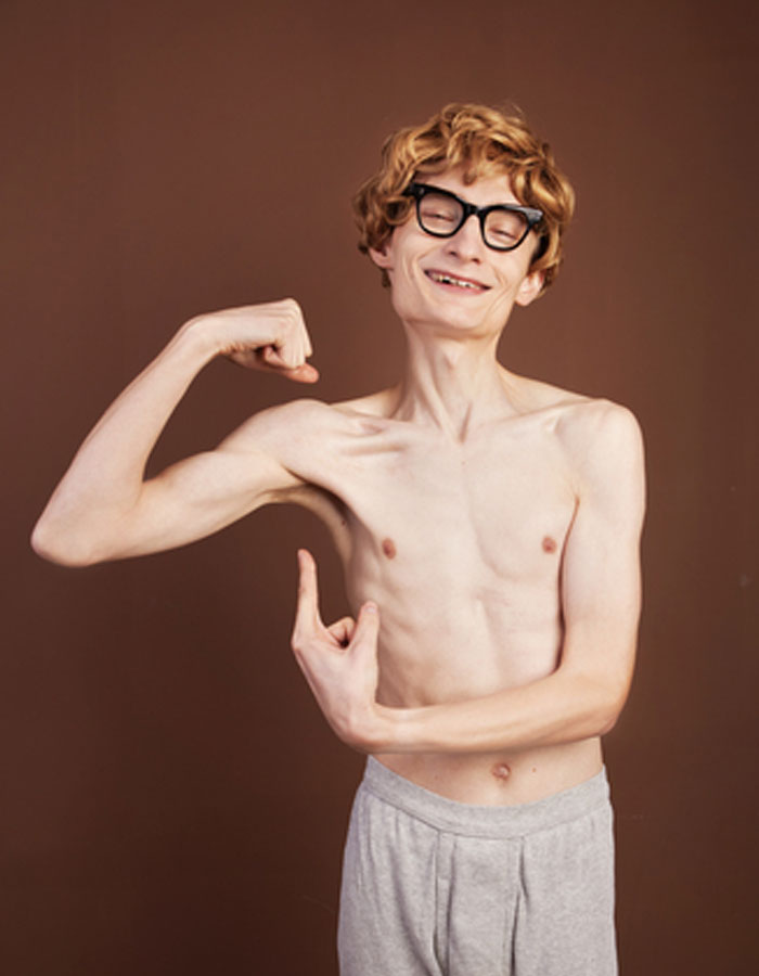A funny image of a skinny man with glasses and a joyful smile striking a pose while flexing his bicep in a playful attempt to show off his muscles. His confident expression contrasts humorously with his thin physique. This image could be used as inspiration for a "funny group chat name" related to fitness, unexpected strength, or lighthearted self-confidence. A funny image of a skinny man with glasses and a joyful smile striking a pose while flexing his bicep in a playful attempt to show off his muscles. His confident expression contrasts humorously with his thin physique. This image could be used as inspiration for a "funny group chat name" related to fitness, unexpected strength, or lighthearted self-confidence.