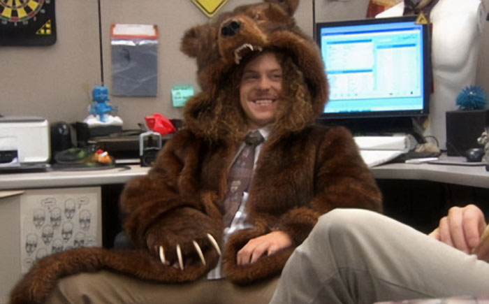 A humorous image of a man sitting in an office cubicle, smiling broadly while wearing a full bear costume with the bear's head acting as a hood. The setting is a typical office environment with computers and documents, contrasting comically with the man's unusual outfit. This image could inspire a "funny group chat name" related to office shenanigans, unique dress codes, or playful workday surprises. A humorous image of a man sitting in an office cubicle, smiling broadly while wearing a full bear costume with the bear's head acting as a hood. The setting is a typical office environment with computers and documents, contrasting comically with the man's unusual outfit. This image could inspire a "funny group chat name" related to office shenanigans, unique dress codes, or playful workday surprises.