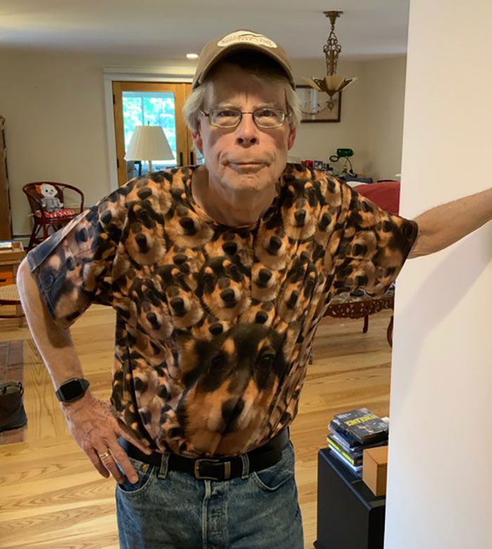 Person in a cap and dog-themed shirt stands indoors, hands on hips, looking directly at the camera. Person in a cap and dog-themed shirt stands indoors, hands on hips, looking directly at the camera.
