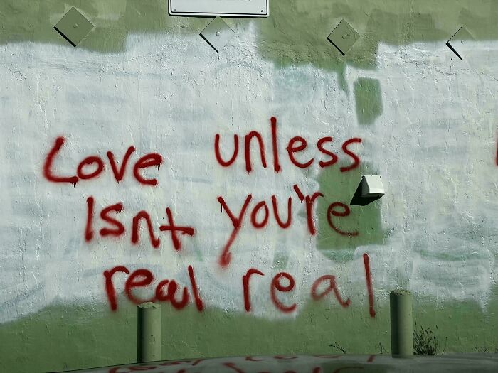 Graffiti message on a wall with a sign fail: "Love Isn't Real Unless You're Real."