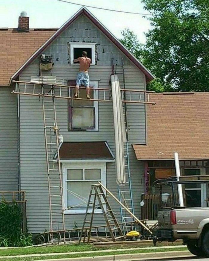 Man standing dangerously on unstable ladder setup outside house, ignoring safety protocol and creating hazardous conditions.