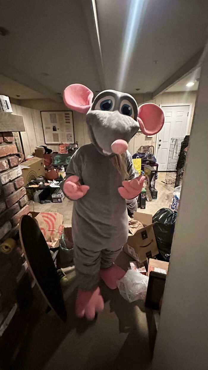 Person in a rat costume standing in a cluttered room, showcasing a surprising thrifting find.