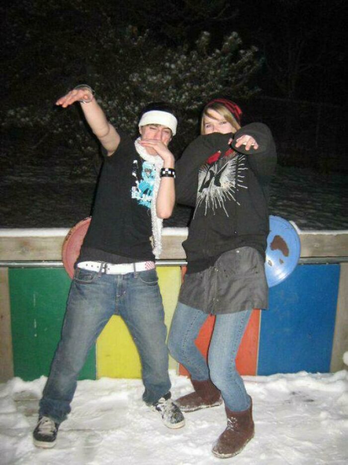 Two people posing playfully in winter attire, embodying blunder years fashion, with colorful background and snow underfoot.
