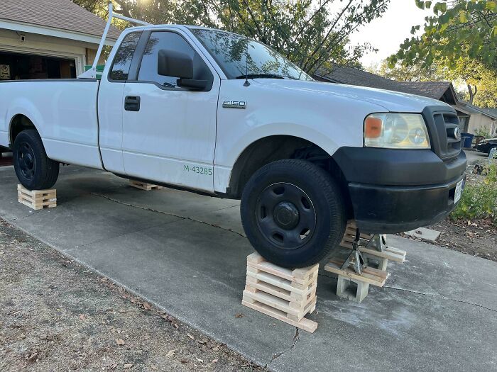 White pickup truck dangerously elevated on unstable wooden and concrete blocks, ignoring safety protocol risking severe accidents.