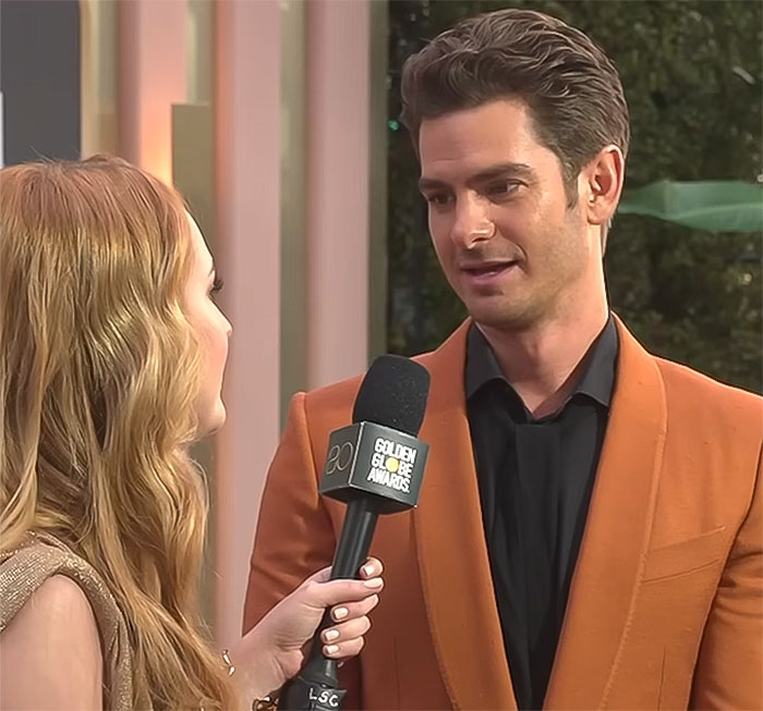 A man in an orange suit and a woman interviewing him at the Golden Globe Awards, focusing on seduction and charm. A man in an orange suit and a woman interviewing him at the Golden Globe Awards, focusing on seduction and charm.