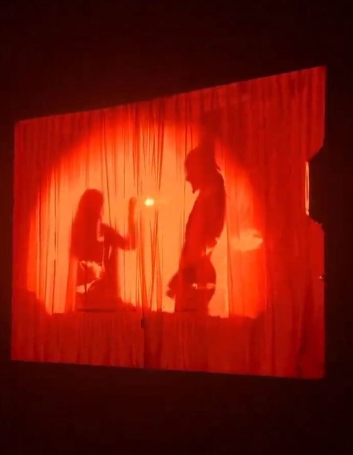 Silhouettes behind a red curtain on stage, sparking controversy. Silhouettes behind a red curtain on stage, sparking controversy.