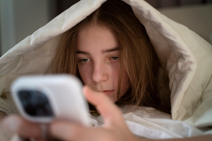 A girl under a blanket looks at a smartphone screen, appearing contemplative. A girl under a blanket looks at a smartphone screen, appearing contemplative.