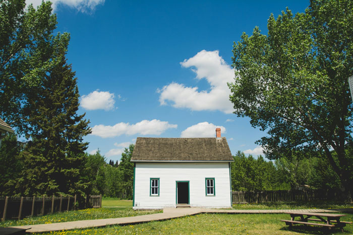 A small white house with a wooden roof surrounded by trees, under a clear blue sky. A small white house with a wooden roof surrounded by trees, under a clear blue sky.