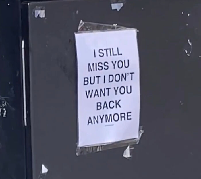 Wholesome message poster on a dark wall in London streets expressing mixed emotions about missing someone.