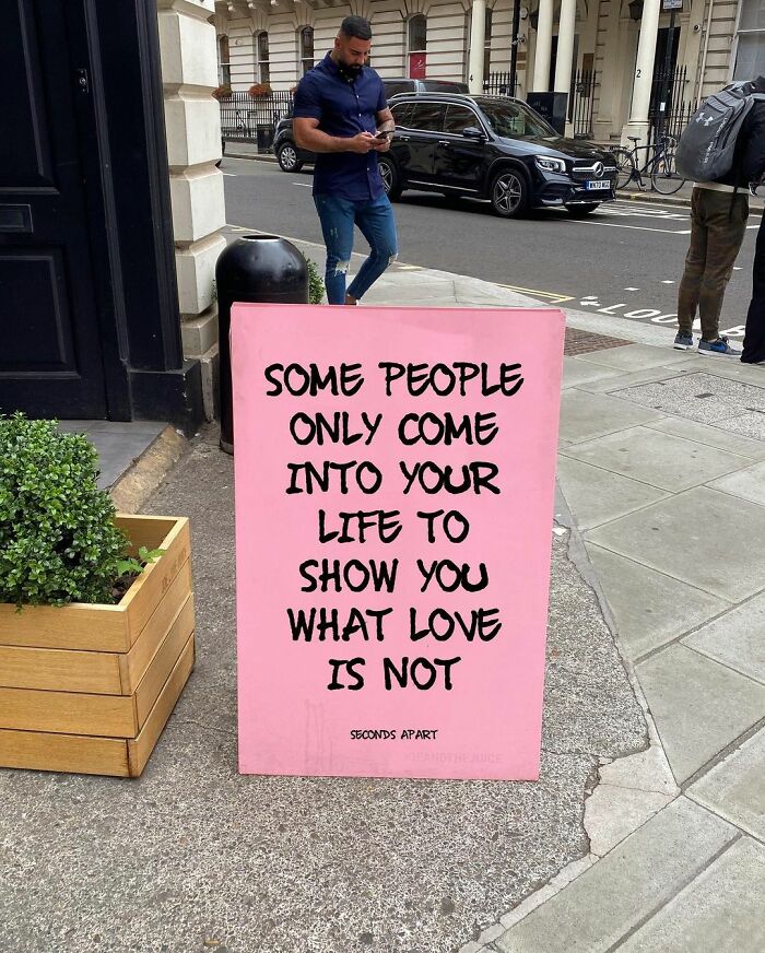 Pink street sign with a wholesome message about love on a London sidewalk, capturing heartfelt messages from city streets.