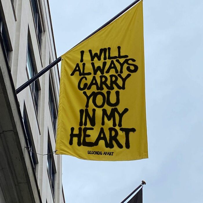 Yellow street banner in London with a wholesome message expressing deep care and carrying someone in heart.