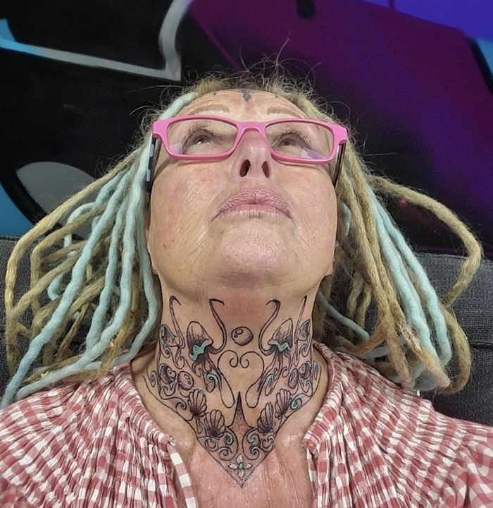 A woman with face tattoos and pink glasses, wearing a red-checkered shirt, looking upwards. A woman with face tattoos and pink glasses, wearing a red-checkered shirt, looking upwards.