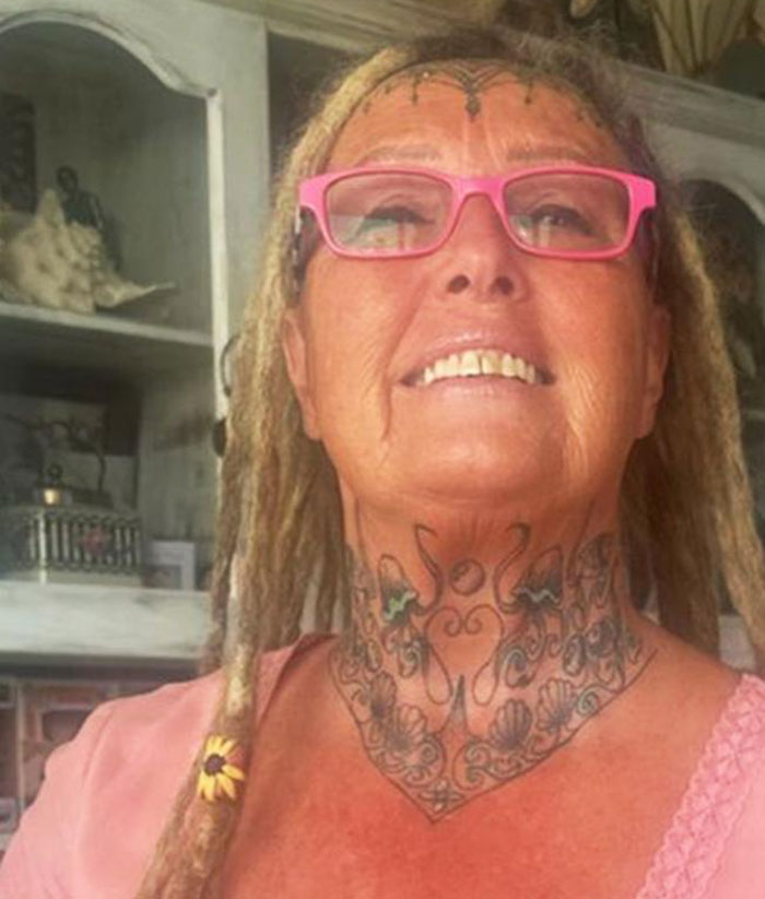 63-year-old woman with face tattoos and pink glasses smiling indoors. 63-year-old woman with face tattoos and pink glasses smiling indoors.