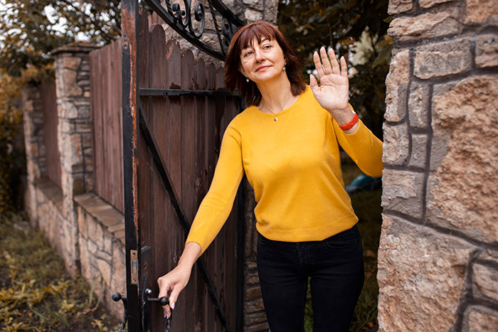 Woman in a yellow sweater waves at a stone gate, related to HOA president and new resident conflict. Woman in a yellow sweater waves at a stone gate, related to HOA president and new resident conflict.