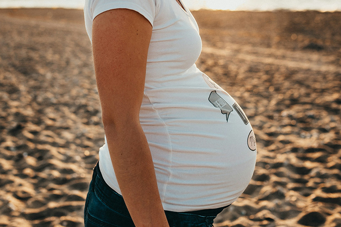 Pregnant woman on a sandy beach, wearing a printed white t-shirt, with a sunset in the background. Pregnant woman on a sandy beach, wearing a printed white t-shirt, with a sunset in the background.