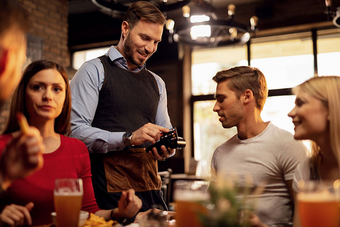 Cashier at a restaurant discreetly adds tip while processing payment for seated patrons. Cashier at a restaurant discreetly adds tip while processing payment for seated patrons.