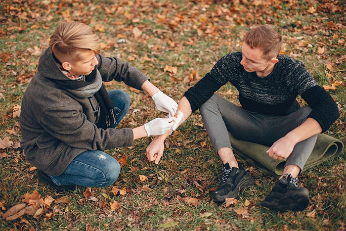 A person bandaging a bleeding employee's arm outdoors on a fall day. A person bandaging a bleeding employee's arm outdoors on a fall day.