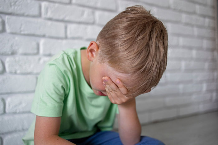 Child in a green shirt sitting against a white brick wall, covering face. Child in a green shirt sitting against a white brick wall, covering face.