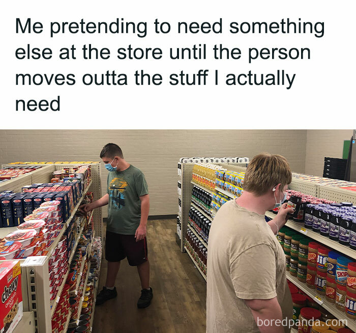 Two people in a grocery store aisle, one pretending to shop to avoid interacting with others.